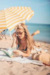 Girl reading a book at the beach under a beach umbrella.