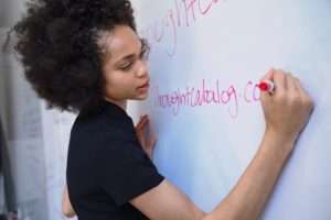 African American female teacher writing on a white board.