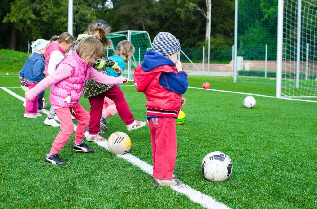 Preschool children on a soccer field practicing kicking soccer balls.