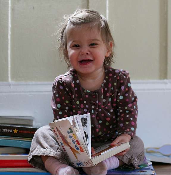 Smiling female toddler with a book in her lap.