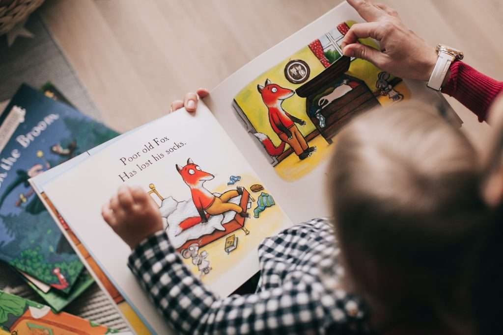 A young male child sitting on a parents lap looking at a picture book with the parent.