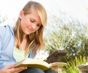 Smiling teen girl reading a book while sitting outside.