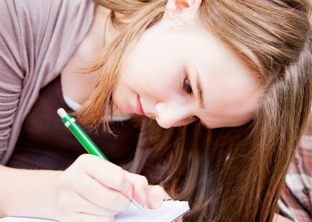 Teen girl writing on a piece of paper.