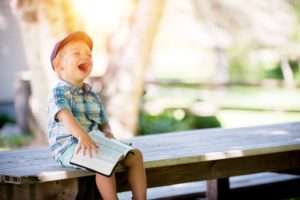 Young boy with a book sitting on a bench.