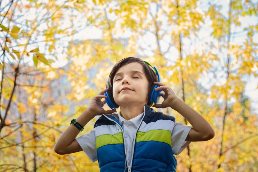 Student listening to headphones while walking in a forest with yellow leaves on the trees.