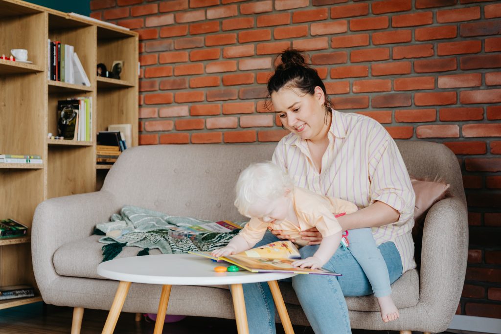 Mother sitting on a couch holding a young child who is looking at a picture book.