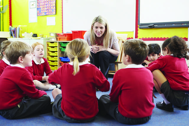 Adult lady talking to a group of children seated on the floor.